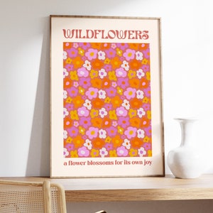 Puede incluir: Una impresión enmarcada con un patrón floral en tonos naranja, rosa y blanco. El texto "WILDFLOWERS" está en la parte superior de la impresión, y el texto "a flower blossoms for its own joy" está en la parte inferior.