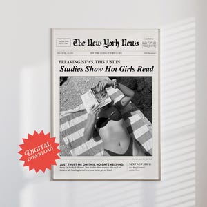 Puede incluir: Una fotografía en blanco y negro de una mujer leyendo un libro en una playa. La foto está enmarcada en un marco negro y tiene el titular "Studies Show Hot Girls Read" de un periódico ficticio llamado "The New York News".