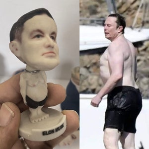 May include: A small, white figurine of Elon Musk with a large head and a small body. The figurine is wearing black shorts and is standing on a white base with the words "Elon Musk" printed on it.
