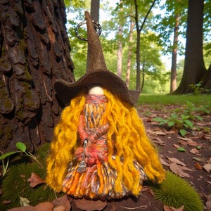 Puede incluir: Una muñeca de gnomo hecha a mano con temática de bruja. El gnomo tiene un sombrero puntiagudo marrón, pelo largo amarillo y un vestido naranja y rojo colorido. Sostiene una pequeña escoba plateada. La muñeca está colocada contra un fondo de un bosque con árboles verdes y follaje.
