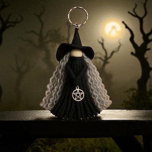 May include: A handmade witch doll keychain with a black hat, dress, and gray hair. The doll has a silver pentacle pendant and a silver keyring. The background features a spooky forest scene with a full moon.