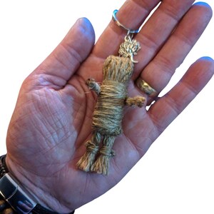 Peut inclure: Un porte-cl&eacute;s poup&eacute;e fait &agrave; la main en ficelle naturelle. La poup&eacute;e est envelopp&eacute;e de ficelle, avec les bras et les jambes attach&eacute;s. Un charm en forme d'arbre de couleur argent&eacute;e est attach&eacute; en haut. La poup&eacute;e est tenue dans une main.