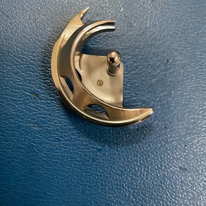 May include: A silver sewing machine foot with a curved shape and a small metal knob on the top.