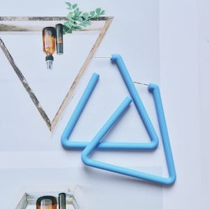 May include: A pair of light blue triangle shaped earrings. The earrings are made of a smooth, matte material.