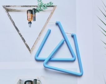 May include: A pair of light blue hoop earrings shaped like triangles. The earrings feature a smooth, matte finish and a simple, geometric design with a standard post-back closure mechanism for securing the jewelry to the earlobe.