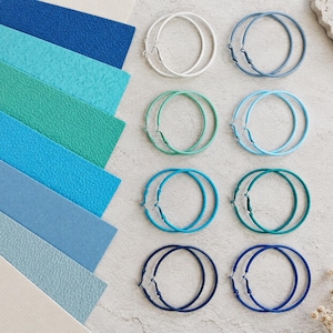 May include: Eight pairs of hoop earrings in various shades of blue, teal, and white, arranged in two columns. Beside them are eight strips of textured material in matching colors, including navy, bright blue, turquoise, and light blue shades.