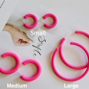 May include: Three pairs of pink hoop earrings in different sizes: small, medium, and large. The earrings are made of a smooth, matte material.