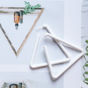 May include: A pair of white triangle hoop earrings. The earrings are made of a thick, white plastic material and are about 3 inches in diameter.