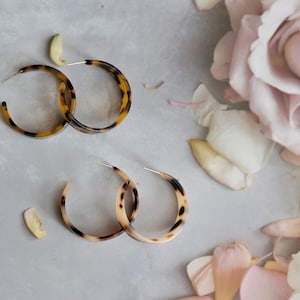 May include: A pair of brown and black tortoise shell hoop earrings. The earrings are made of plastic and have a smooth finish.