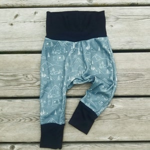 May include: A pair of blue and black baby trousers with a camping themed print. The trousers have a black waistband and black cuffs.
