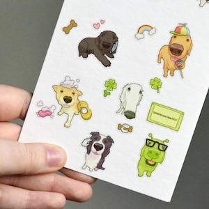 May include: A sticker sheet featuring various cartoon illustrations including a dark brown dog, a golden dog with a colorful hat and lollipop, a dog with soap bubbles, a white dog, a black and white dog, a green creature with glasses, and a note.