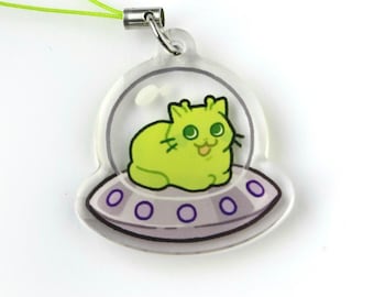 May include: A clear acrylic charm featuring a lime green cat inside a spaceship. The cat has a happy expression and is sitting on a purple and gray saucer. The charm has a silver clasp and a green string.