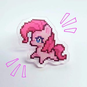 May include: Pinkie Pie from My Little Pony is depicted in a pixelated style on a clear acrylic charm. The charm is pink and white and features a pink mane and tail.