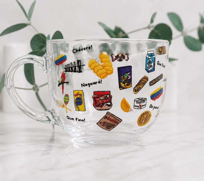 May include: Clear glass mug decorated with colorful Venezuelan food and cultural icons. The mug features images of snacks, flags, and phrases like "Ch&eacute;vere!" and "Naguar&aacute;!" A perfect gift for anyone who loves Venezuela.
