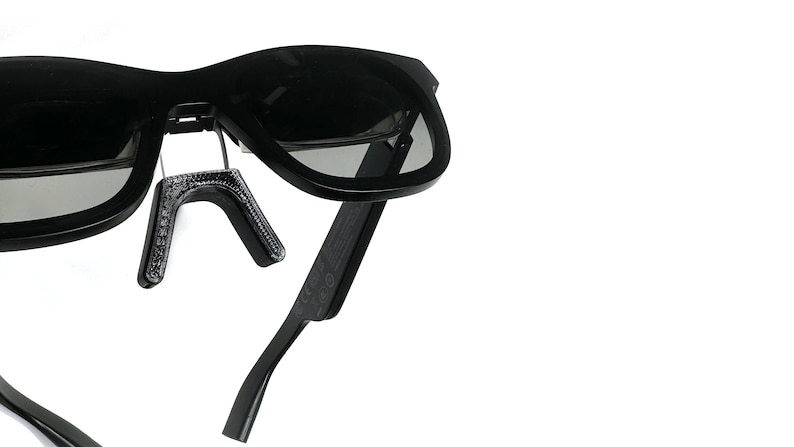May include: Black sunglasses with a flexible, adjustable arm. The sunglasses have a dark gray lens and a black frame.