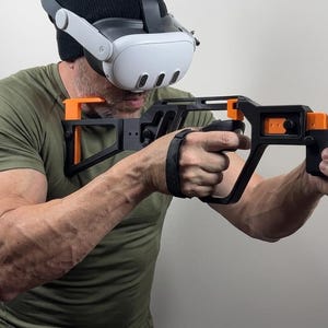 May include: A black and orange 3D-printed VR gun stock controller mount designed for virtual reality gaming. The frame features a skeletal structure with orange accents, holding two black VR controllers in a rifle-like configuration for stability.