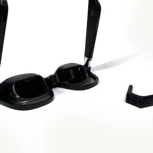May include: Black foldable sunglasses with a silver hinge and a separate black nose piece.