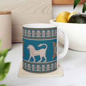 May include: White ceramic mug with a blue and brown design featuring a stylized lion and geometric patterns. The mug has a handle on the right side.