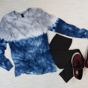 Może przedstawiać: Długi rękaw w kolorze niebieskim i szarym z efektem tie-dye, czarne legginsy i para bordowych butów Vans.