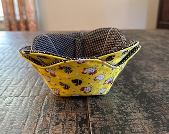 May include: A yellow fabric bowl with a black and white chicken print. The bowl is lined with a black and white checkered fabric.