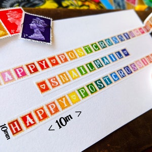 May include: A white card with colorful washi tape featuring the words "Happy Postcrossing", "Snail Mail", and "Happy Postcrossing" with a heart symbol between each word. The tape is 10mm wide and the card also includes the text "< 10m".