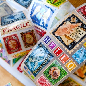 Puede incluir: Un rollo de pegatinas coloridas con patrones y una variedad de dise&ntilde;os, que incluyen un caracol, un pez, un p&aacute;jaro y una mano sosteniendo una carta. Las pegatinas est&aacute;n dispuestas en espiral y tienen un acabado brillante. El texto en las pegatinas dice "HELLO", "SPECIAL DELIVERY", "AIRMAIL", "FINGERS CROSSED" y "POSTAGE".