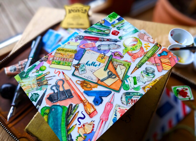 Puede incluir: Una tarjeta blanca con una ilustraci&oacute;n colorida de varios art&iacute;culos de papeler&iacute;a, incluyendo bol&iacute;grafos, l&aacute;pices, tijeras, cinta adhesiva y una libreta con la palabra "&iexcl;hola!" escrita en ella.