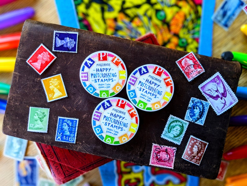 May include: A collection of colorful round stickers with the text "Magcherie - Happy Postcrossing Stamps" and a variety of colorful postage stamps. The stamps feature different designs, including a portrait of a woman, a bird, and a floral pattern.