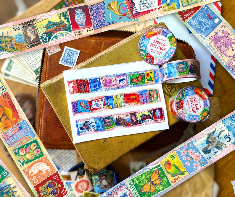 May include: Assortment of colorful washi tapes featuring vintage postage stamps with various designs, including flowers, animals, and buildings. The tapes are rolled up and arranged on a brown leather surface with other decorative items.