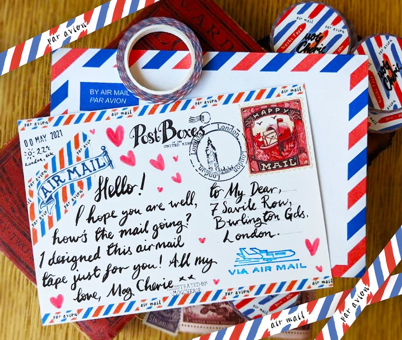 May include: A white envelope with red and blue stripes, decorated with washi tape and hearts. The envelope has a stamp with the words "Happy Mail" and a handwritten message that reads "Hello! I hope you are well, how's the mail going? I designed this airmail tape just for you! All my love, Mag Cherie."