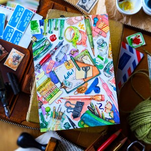 Puede incluir: Una ilustraci&oacute;n acuarela de una variedad de art&iacute;culos de papeler&iacute;a coloridos, que incluyen l&aacute;pices, bol&iacute;grafos, tijeras, cinta adhesiva y una peque&ntilde;a libreta con la palabra "&iexcl;hola!" escrita en ella.