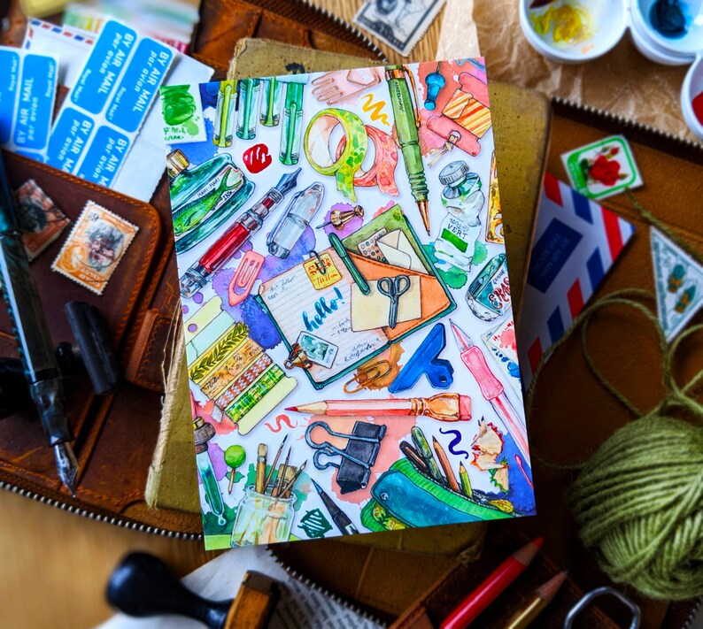 Puede incluir: Una ilustraci&oacute;n acuarela de una variedad de art&iacute;culos de papeler&iacute;a coloridos, que incluyen l&aacute;pices, bol&iacute;grafos, tijeras, cinta adhesiva y una peque&ntilde;a libreta con la palabra "&iexcl;hola!" escrita en ella.