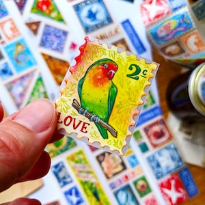 Puede incluir: Una pegatina ilustrada colorida de un par de tortolitos posados en una rama. La pegatina tiene un fondo amarillo con hojas verdes y la palabra "LOVE" en letras rojas. La pegatina tambi&eacute;n tiene un sello de 2c en la esquina superior derecha.