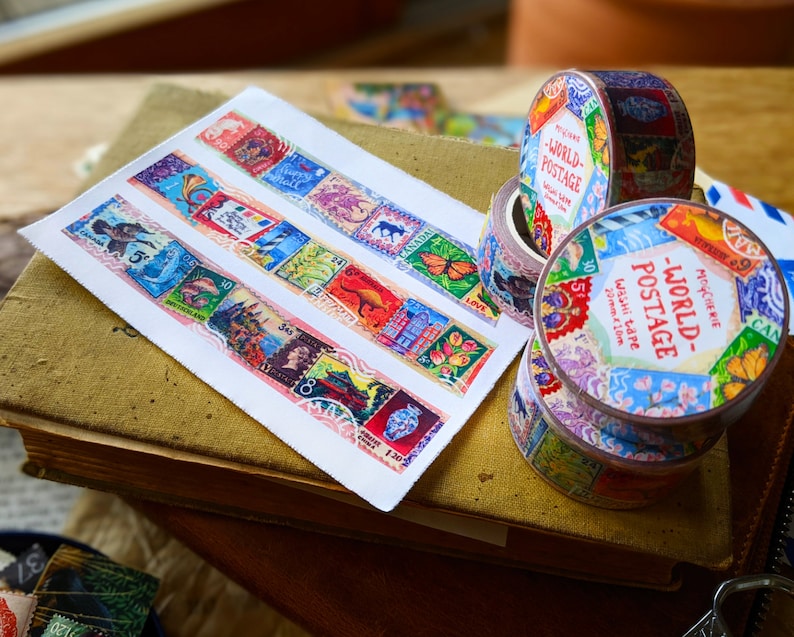 May include: Two rolls of colorful washi tape with a vintage postage stamp design. The tape is labeled "World Postage" and features a variety of stamps from different countries. The tape is 20mm wide and 10 meters long.