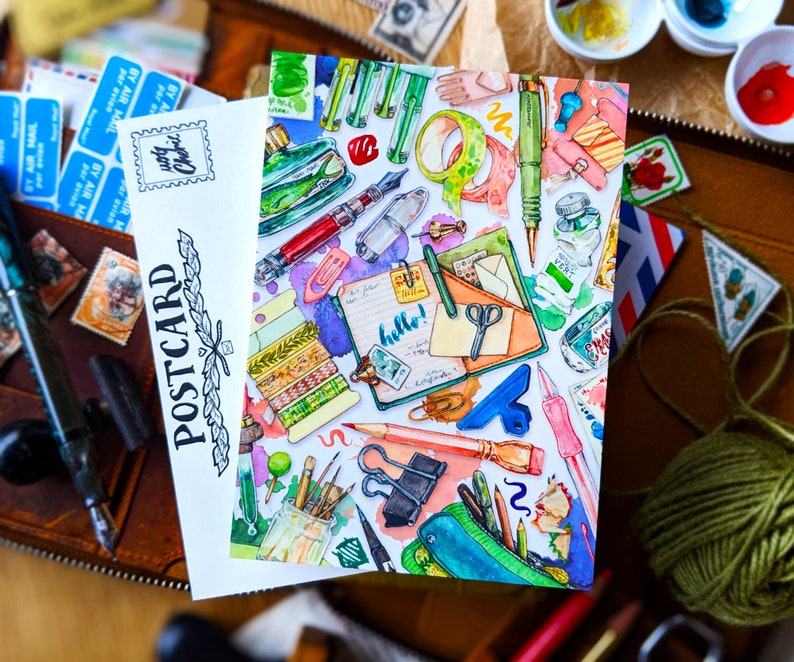 Puede incluir: Una ilustraci&oacute;n de acuarela de una postal con una variedad de art&iacute;culos de papeler&iacute;a coloridos, que incluyen bol&iacute;grafos, l&aacute;pices, tijeras, cinta adhesiva y una libreta con la palabra "&iexcl;hola!" escrita en ella.