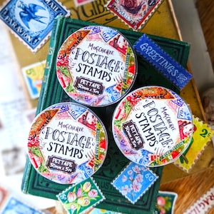 Puede incluir: Tres rollos de cinta washi colorida con un dise&ntilde;o de sello de correos vintage. La cinta est&aacute; etiquetada "Mogcherie Postage Stamps Pettape 50mm x 5m".