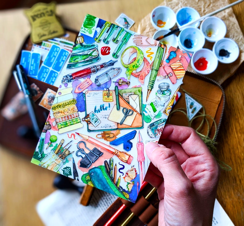 Puede incluir: Una ilustraci&oacute;n acuarela de una variedad de art&iacute;culos de papeler&iacute;a, que incluyen bol&iacute;grafos, l&aacute;pices, tijeras, cinta adhesiva y una libreta con la palabra "&iexcl;hola!" escrita en ella. La ilustraci&oacute;n est&aacute; sobre un fondo blanco y tiene un estilo colorido y caprichoso.