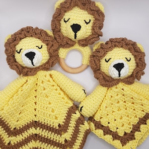 Puede incluir: Tres juguetes de león de crochet en amarillo y marrón. Un león es un sonajero con un anillo de madera. Los otros dos leones están unidos a mantas con rayas marrones y amarillas.