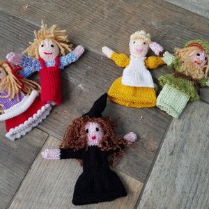 May include: Five knitted finger puppets, each with a different character and colour. The puppets include a girl with red hair and a red dress, a girl with blonde hair and a yellow dress, a girl with blonde hair and a purple dress, a girl with brown hair and a black dress, and a man with blonde hair and a green shirt.