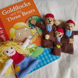 May include: A set of finger puppets featuring Goldilocks and the three bears. The puppets are made of knitted fabric and are brown, red, and blue. The book "Goldilocks and the Three Bears" is also pictured. The book has a red ladybug on the cover and the words "Read it you" are visible.