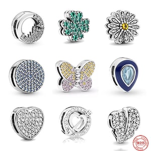 May include: Nine silver charm bracelet clips with various designs, including a heart, a butterfly, a flower, a four-leaf clover, and a circle. Each clip is adorned with sparkling clear, blue, green, and yellow crystals.
