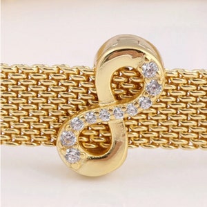 May include: A gold infinity charm with clear cubic zirconia stones set around the edges. The charm is on a gold mesh bracelet.