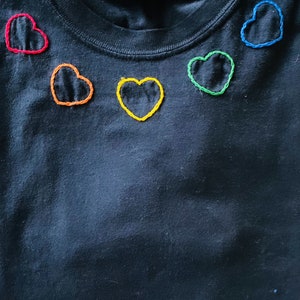 Black 100 % cotton tshirt with rainbow hand embroidered hearts across the neck