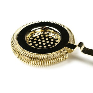 May include: Gold cocktail strainer with a spring-coil design and a handle. The strainer has a fine mesh to remove ice and other solids from cocktails.
