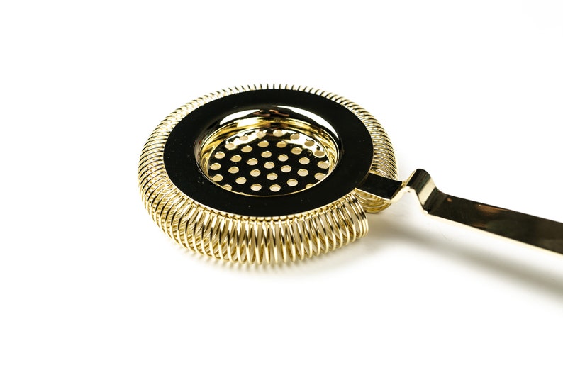 May include: Gold cocktail strainer with a spring-coil design and a handle. The strainer has a fine mesh to remove ice and other solids from cocktails.