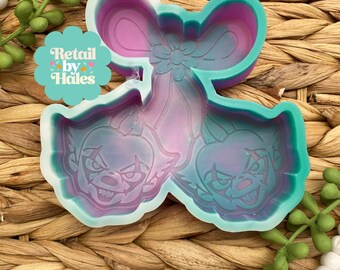 May include: A multi-colored silicone mold featuring two clown faces and a bow design. The mold is in shades of pink, purple, and teal. The text "Retail by Hales" is visible in the image.