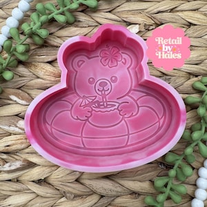 May include: A pink silicone mold in the shape of a bear in an inner tube, holding a drink with a straw. The bear has a flower on its head. The mold is for crafting and has the text "Retail by Hales".