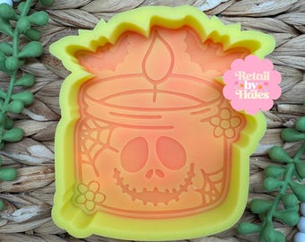 May include: A bright yellow silicone mold featuring a candle in a jar design with a skull face, spider webs, flowers, and bats. The mold has a pink circular logo sticker with the text Retail by Hales printed in white and pink lettering.