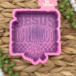 May include: A pink silicone mold with the text "JESUS IS MY BOO" in a playful font, along with a ghost graphic. The mold has a checkered pattern at the bottom and is surrounded by a decorative border. The image includes a pink label that says "Retail by Hales".
