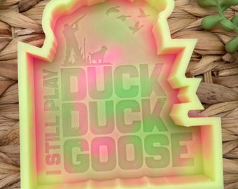 May include: A yellow and pink silicone mold with the text "I still play duck duck goose" and a silhouette of a hunter with a dog and ducks flying overhead.